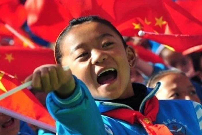 Chinese child standing next to a closed Chinese flag